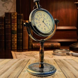 May include: An antique-style clock with a round face and Roman numerals. The clock is set in a dark metal frame and mounted on a decorative stand. The clock's face is cream-colored, and the hands are black. The stand is made of wood and metal.