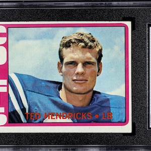May include: A 1972 Topps football card featuring Ted Hendricks of the Colts. The card has a pink border with the word "COLTS" in large white letters. The card is graded EX 5 by SGC and encased in a protective holder.