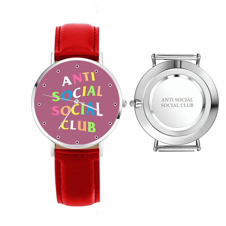 Puede incluir: Un reloj de pulsera con correa de cuero rojo y esfera redonda. La esfera del reloj es de color morado claro con las palabras "ANTI SOCIAL SOCIAL CLUB" en letras coloridas. La parte trasera del reloj es plateada con las palabras "ANTI SOCIAL SOCIAL CLUB".