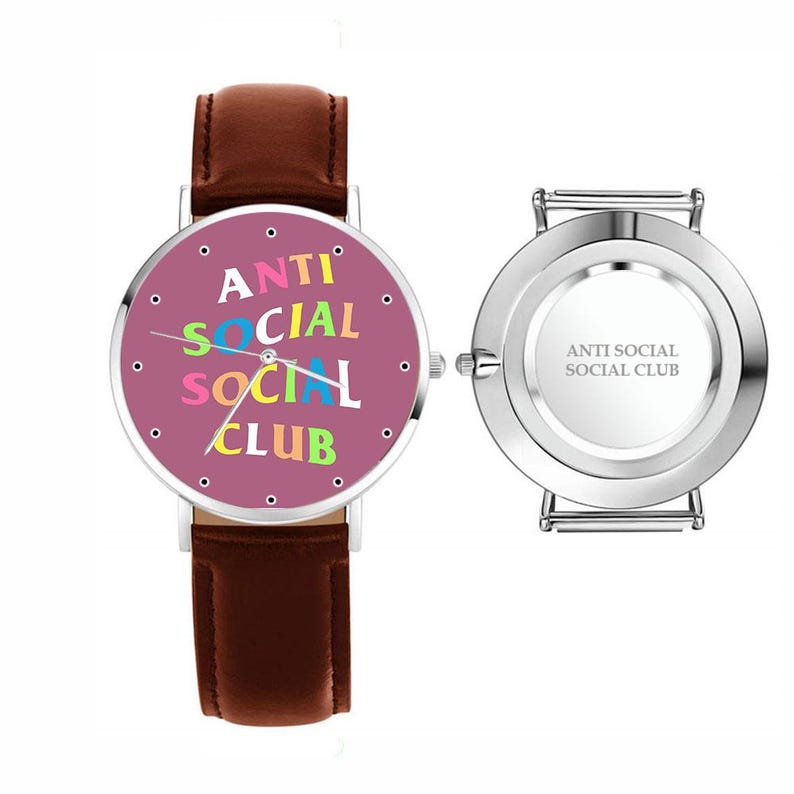 Puede incluir: Reloj de pulsera con correa de cuero marr&oacute;n y caja plateada. La esfera malva muestra el texto "ANTI SOCIAL SOCIAL CLUB" en colores vivos. La parte trasera del reloj tambi&eacute;n tiene el texto "ANTI SOCIAL SOCIAL CLUB".