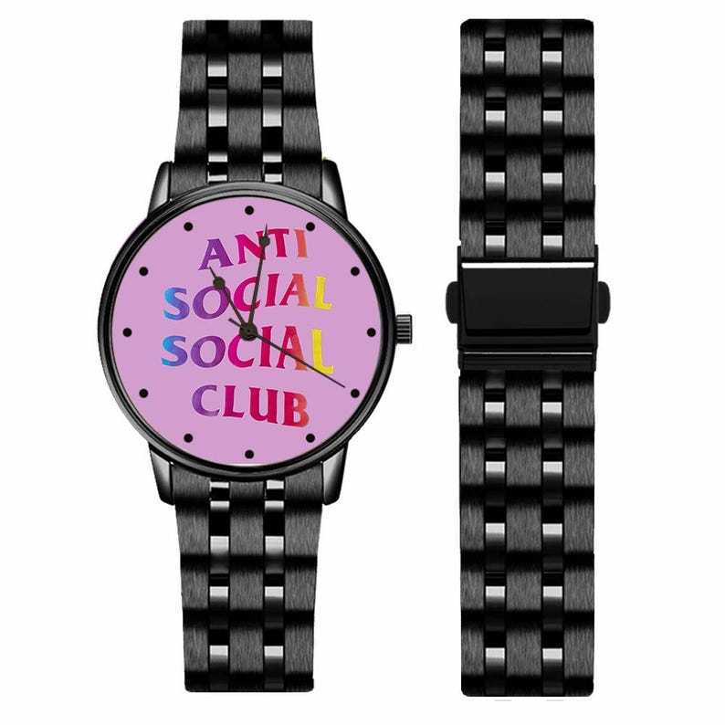 May include: Black wristwatch with a round face and matching band. The watch face is light pink with the words "ANTI SOCIAL SOCIAL CLUB" in colorful text. The band is made of linked metal.