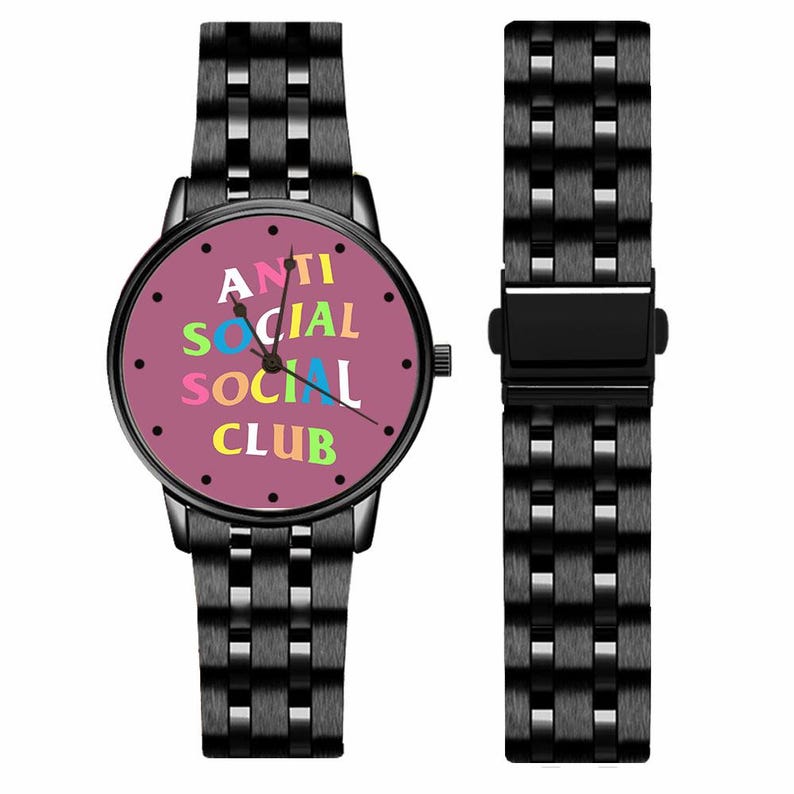 Puede incluir: Reloj de pulsera negro con esfera redonda y correa a juego. La esfera del reloj es de color rosa polvoriento y muestra las palabras "ANTI SOCIAL CLUB" en letras de colores.