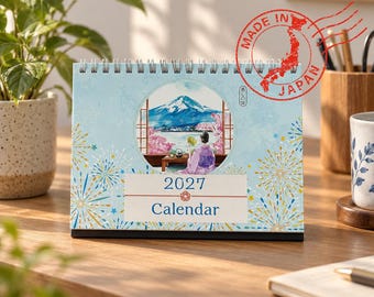 May include: A 2027 desk calendar with a spiral binding, featuring a light blue cover with gold and blue firework illustrations. The center displays a circular watercolor scene of Mount Fuji, cherry blossoms, and a person in a kimono.