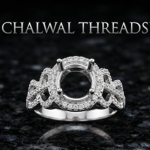 May include: A silver-toned ring setting featuring a central circular mount surrounded by a halo of small clear stones. The band displays an intricate, openwork lattice design encrusted with additional small stones. The text CHALWAL THREADS appears above.