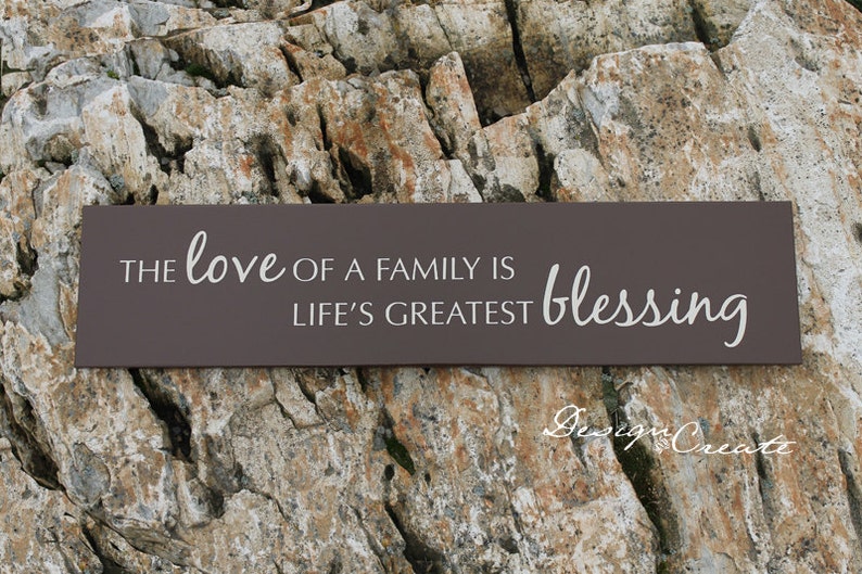 May include: A brown wooden sign with white text that reads "The love of a family is life's greatest blessing".