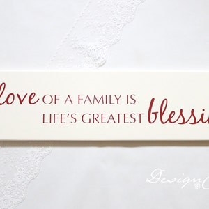 May include: White wooden sign with red lettering that reads "The love of a family is life's greatest blessing".