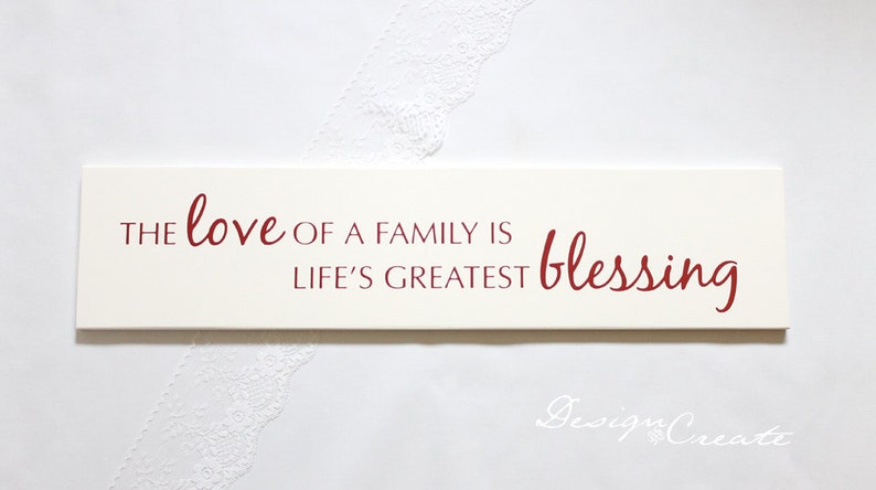 May include: White wooden sign with red lettering that reads "The love of a family is life's greatest blessing".