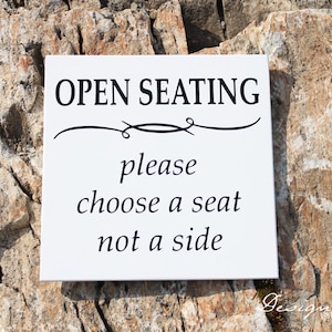 May include: White sign with black text that reads "OPEN SEATING please choose a seat not a side".