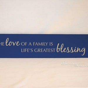 May include: A blue wooden sign with the text "The love of a family is life's greatest blessing" in white lettering.