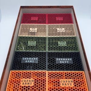 May include: A selection of coloured, honeycomb-patterned containers in a cardboard box. The containers are labelled with country and military branch names, such as "UK ARMY" and "GERMANY NAVY". Colours include red, beige, green, black, and orange.