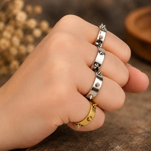 May include: A set of four metal rings worn on the fingers, each featuring a band with evenly spaced conical spikes. Three rings have a polished silver-tone finish, while the bottom ring has a gold-tone finish. The text Prao Jewels is visible.