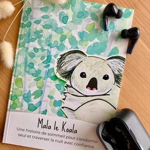 Peut inclure: Un livre pour enfants intitulé "Mala le Koala" avec une illustration de koala et un fond aquarelle vert et bleu. Des écouteurs sans fil noirs sont placés sur le livre, et un étui de chargement est ouvert à côté. Le texte dit : "Une histoire de sommeil pour s'endormir seul et traverser la nuit avec confiance."