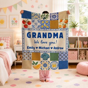 May include: A rectangular throw blanket featuring a patchwork design of blue and white Mediterranean-style tiles, tomatoes, oranges, and a seashell. The center text reads GRANDMA We love you! Emily Michael Andrew in blue lettering.