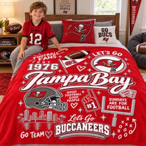 May include: A red fleece blanket featuring Tampa Bay Buccaneers graphics, including a football helmet, a goalpost, a foam finger, and the text 'Tampa Bay', 'Let's Go Buccaneers', 'Football Fans Est 1976', and 'Sundays Are For Football'.