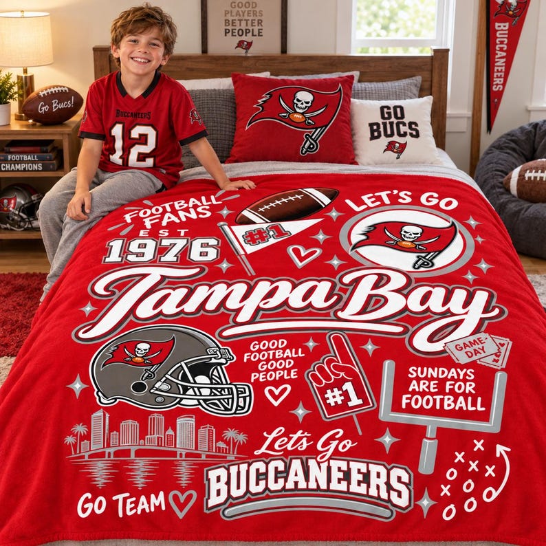 May include: A red fleece blanket featuring Tampa Bay Buccaneers graphics, including a football helmet, a goalpost, a foam finger, and the text 'Tampa Bay', 'Let's Go Buccaneers', 'Football Fans Est 1976', and 'Sundays Are For Football'.