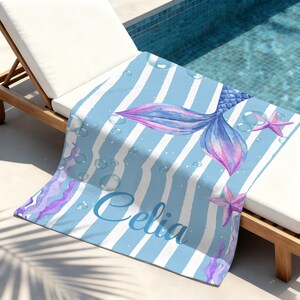 May include: A blue and white striped beach towel featuring a watercolor mermaid tail in shades of blue and purple. The towel includes the name "Celia" in script and starfish accents.
