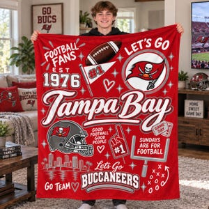 May include: A red fleece blanket featuring Tampa Bay Buccaneers graphics, including a football, a skull logo, a helmet, a goalpost, and text reading Football Fans Est 1976, Tampa Bay, Good Football Good People, and Sundays Are For Football.