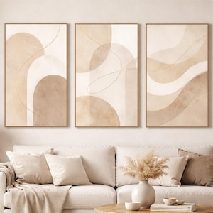 May include: Three framed abstract art prints in beige and brown tones. The artwork features organic shapes and lines. The prints are displayed above a white sofa with beige cushions and a wooden coffee table, creating a stylish interior design.