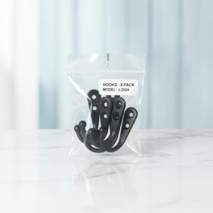 Puede incluir: Una bolsa de pl&aacute;stico transparente resellable que contiene ocho ganchos de metal negro mate. Una etiqueta rectangular blanca en la parte frontal de la bolsa muestra el texto negro: HOOKS - 8 PACK MODEL: J-2024. Cada gancho tiene un dise&ntilde;o curvo.