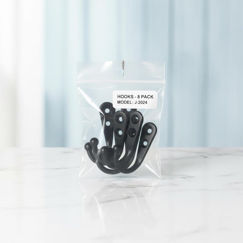 Puede incluir: Una bolsa de pl&aacute;stico transparente resellable que contiene ocho ganchos de metal negro mate. Una etiqueta rectangular blanca en la parte frontal de la bolsa muestra el texto negro: HOOKS - 8 PACK MODEL: J-2024. Cada gancho tiene un dise&ntilde;o curvo.