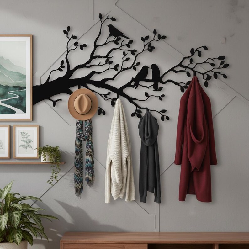 Puede incluir: Un perchero de pared de metal negro con forma de rama de &aacute;rbol con hojas y tres p&aacute;jaros posados. El perchero sostiene un sombrero fedora beige, una bufanda estampada, un su&eacute;ter blanco, una sudadera negra y un abrigo largo granate.
