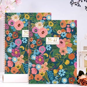 May include: Two spiral-bound monthly planners with a dark teal background and a vibrant floral pattern in pink, orange, yellow, and blue. The text "26-27 MONTHLY PLANNER" is visible on the cover.