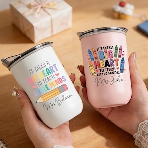 May include: Two stainless steel tumblers, one white and one pink, with black lids. The white tumbler has the text "IT TAKES A BIG HEART TO TEACH LITTLE MINDS" and a pencil graphic. The pink tumbler has the same text and crayon graphics.