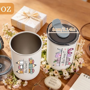 May include: Two white insulated tumblers with black lids, one open and one closed, decorated with teacher-themed graphics. One tumbler is labeled "Mrs. Farnet" and the other "Mrs. Cruse". The tumblers are 4.72 inches tall and 3.14 inches wide.