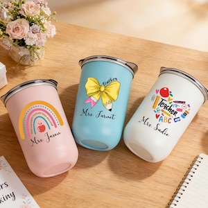 May include: Three insulated tumblers with teacher-themed designs. One is pink with a rainbow and apple, another is light blue with a bow and pencil, and the third is white with school supplies. Each has a name.