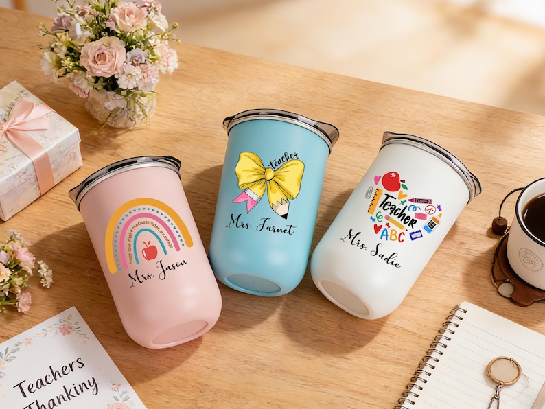 May include: Three insulated tumblers with teacher-themed designs. One is pink with a rainbow and apple, another is light blue with a bow and pencil, and the third is white with school supplies. Each has a name.