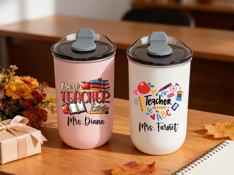 May include: Two insulated tumblers with black lids and gray flip-top closures. One is pink with "Best Teacher Ever" text and the other is white with a heart-shaped teacher graphic. Both have teacher's names.