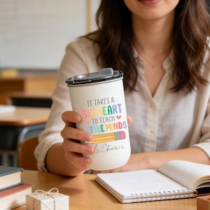 May include: A white travel mug with a black lid, featuring the text "IT TAKES A BIG HEART TO TEACH LITTLE MINDS" in colorful letters and a pencil illustration. The mug is personalized with the name "Ms. Charis".