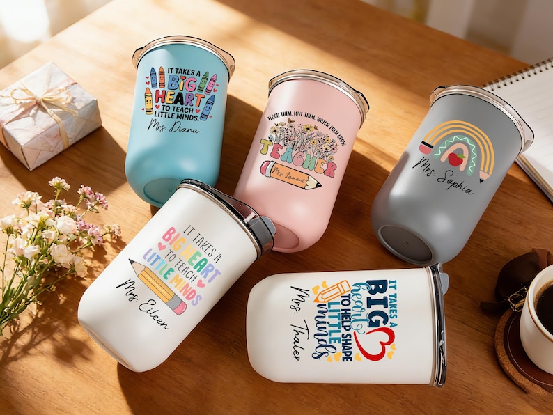 May include: An assortment of insulated tumblers in various colors, including blue, pink, gray, and white. Each tumbler features a design with text and graphics related to teaching, such as pencils, rainbows, and the phrase "It takes a big heart to teach little minds."