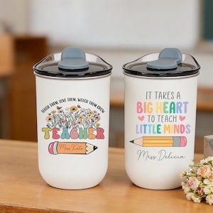 May include: Two white travel mugs with black lids and gray flip-top closures. One mug has the text "Teach them, love them, watch them grow TEACHER" with a pencil graphic. The other mug says "It takes a big heart to teach little minds."