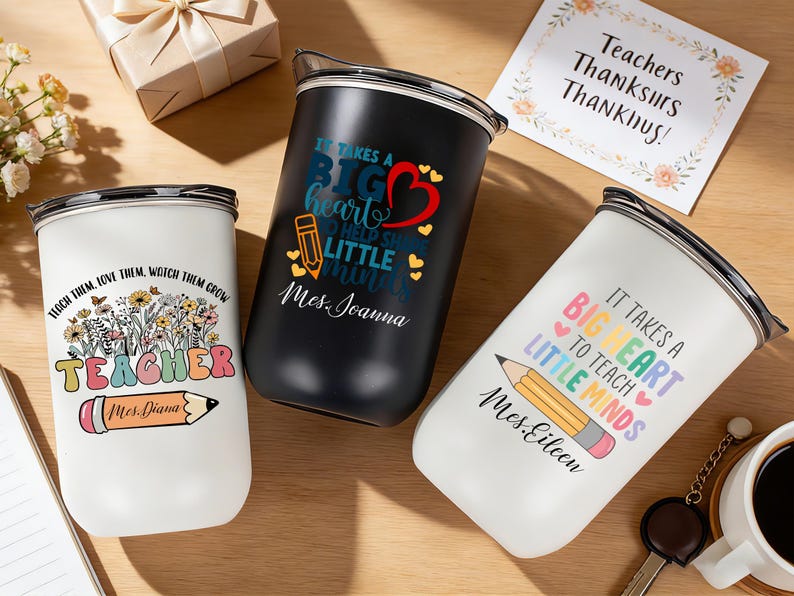 May include: Three insulated tumblers with teacher-themed designs. One white tumbler has the text "TEACHER" and a pencil graphic. A black tumbler has the text "It takes a BIG heart" and a red heart graphic. A white tumbler has the text "It takes a BIG heart to teach little minds."