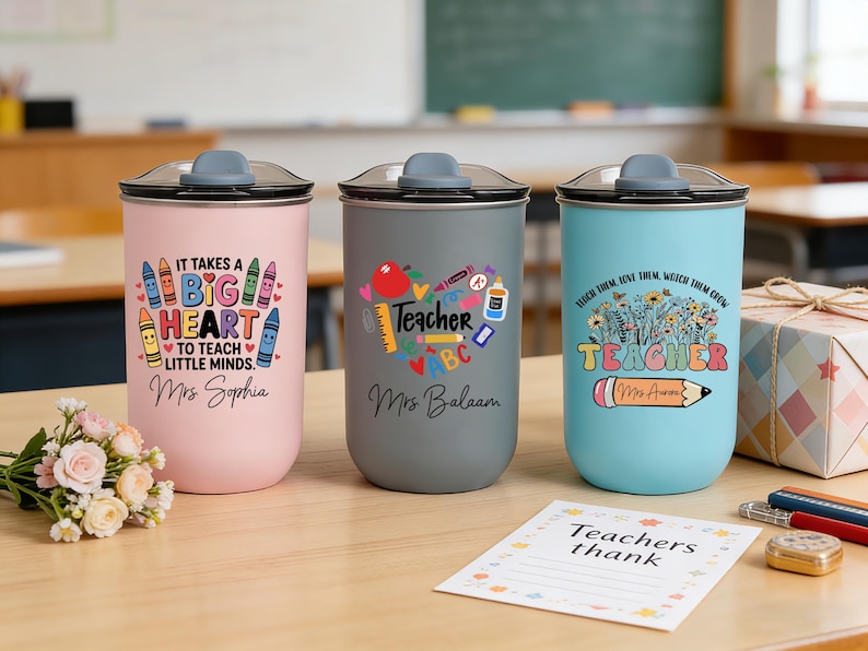 May include: Three insulated tumblers with lids, each featuring a teacher-themed design. One is pink with a crayon graphic and the text "It takes a big heart to teach little minds." The second is gray with a heart graphic and the word "Teacher." The third is blue with a floral graphic and the word "Teacher."