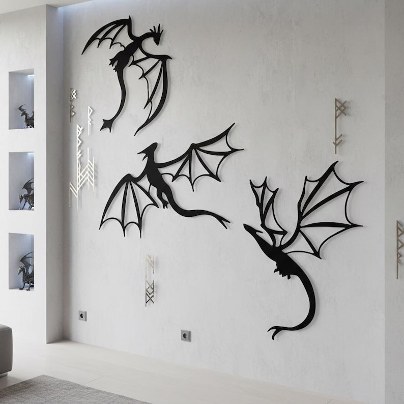 May include: Set of three black metal dragon wall decorations. The dragons, with detailed wing designs, are mounted on a white wall. The artwork features stylized dragons with curved tails. Decorative wall art.