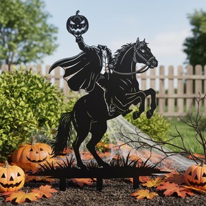 Könnte beinhalten: Schwarze Metall-Silhouette des kopflosen Reiters auf einem steigenden Pferd, das einen Kürbis hält. Die Halloween-Dekoration befindet sich in einem Garten mit Kürbissen, Blättern und einem Zaun im Hintergrund.