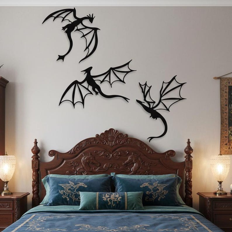 May include: Three black dragon wall art pieces with outstretched wings are mounted on a white wall above a bed. The bed has a dark brown, ornate headboard, blue pillows, and a blue bedspread. Two lamps sit on bedside tables on either side of the bed.