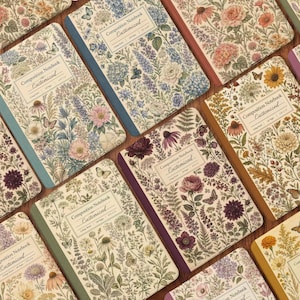 May include: A collection of composition notebooks featuring botanical illustrations of various flowers, leaves, and butterflies. Each notebook has a central label with the text Composition Notebook Customized, College Ruled, 120 Pages, 9.75 x 7.5.