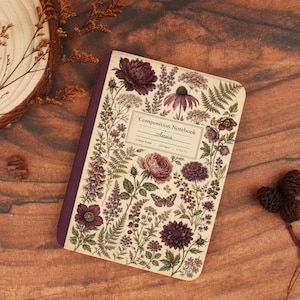 May include: A composition notebook with a cream-colored cover featuring a botanical illustration of purple and dark red flowers, ferns, and a butterfly. A central rectangular label displays the text: Composition Notebook, Anna, College Ruled, 120 Pages, 9.75 x 7.5.