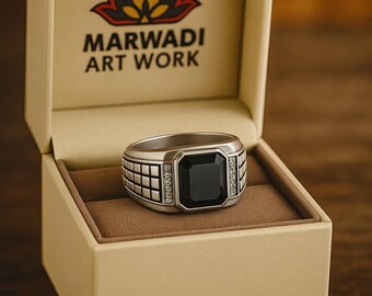 May include: A silver ring with a large, square black gemstone, set in a rectangular design with small accent stones. The ring is displayed in a beige box with the text "MARWADI ART WORK" and a logo.