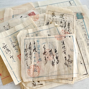May include: A collection of vintage off-white paper documents featuring handwritten Japanese calligraphy in black ink, blue printed borders, and red circular stamps. The aged, translucent sheets are layered, displaying various dates and characters.