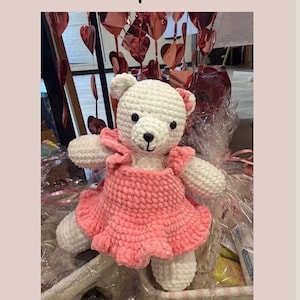 Op de afbeelding: Een wit gehaakte ijsbeer knuffel genaamd Luna the polarbear, gekleed in een roze jurk met ruches en een kleine roze bloem als accessoire op het hoofd. De tekst Luna the polarbear en Design by Sullysdreamycorner is zichtbaar op de afbeelding.