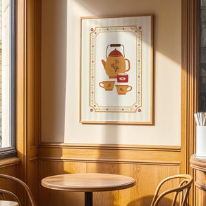 May include: A framed print depicting a teapot, two teacups, and a small jar in a warm colour palette. The illustration has floral details. The print is displayed in a cafe setting with wooden tables and chairs.
