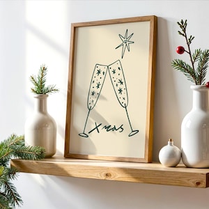 Peut inclure: Une affiche encadrée avec un dessin de deux coupes de champagne et le mot "Xmas". L'affiche est posée sur une étagère en bois, avec deux vases blancs, une petite boule et des brins de verdure.