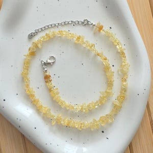 Peut inclure: Un collier ras-du-cou composé de petites pierres de citrine jaune-orangé irrégulières. Le collier est doté d'une chaîne et d'un fermoir argentés. Les pierres sont enfilées pour former un bijou simple et élégant.