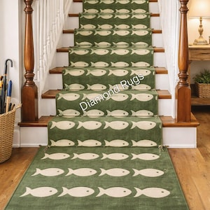 May include: Green stair runner with a repeating pattern of white fish. The runner is installed on wooden stairs with a matching rug at the base. The stair runner has a fringed edge.