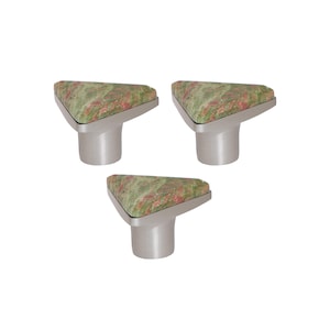 May include: Three cabinet knobs with a triangular top featuring a green and red speckled pattern. The knobs have a brushed silver finish and a cylindrical base. These decorative knobs are suitable for furniture.