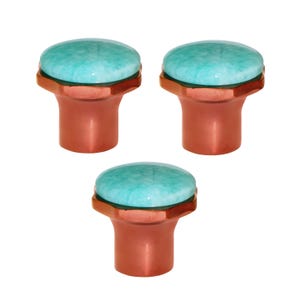 May include: Three cabinet knobs. Each has a copper-coloured base and a round, light blue stone top. The knobs are designed for drawers or cabinet doors. The stone has a mottled appearance. Suitable for use in the UK.